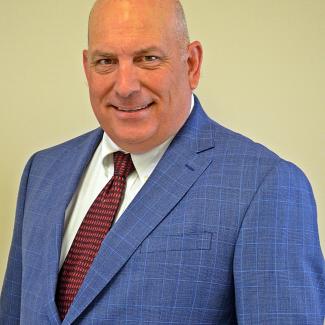 A headshot of Mr. Stuart Smith wearing a blue suit with a white shirt and red tie. 